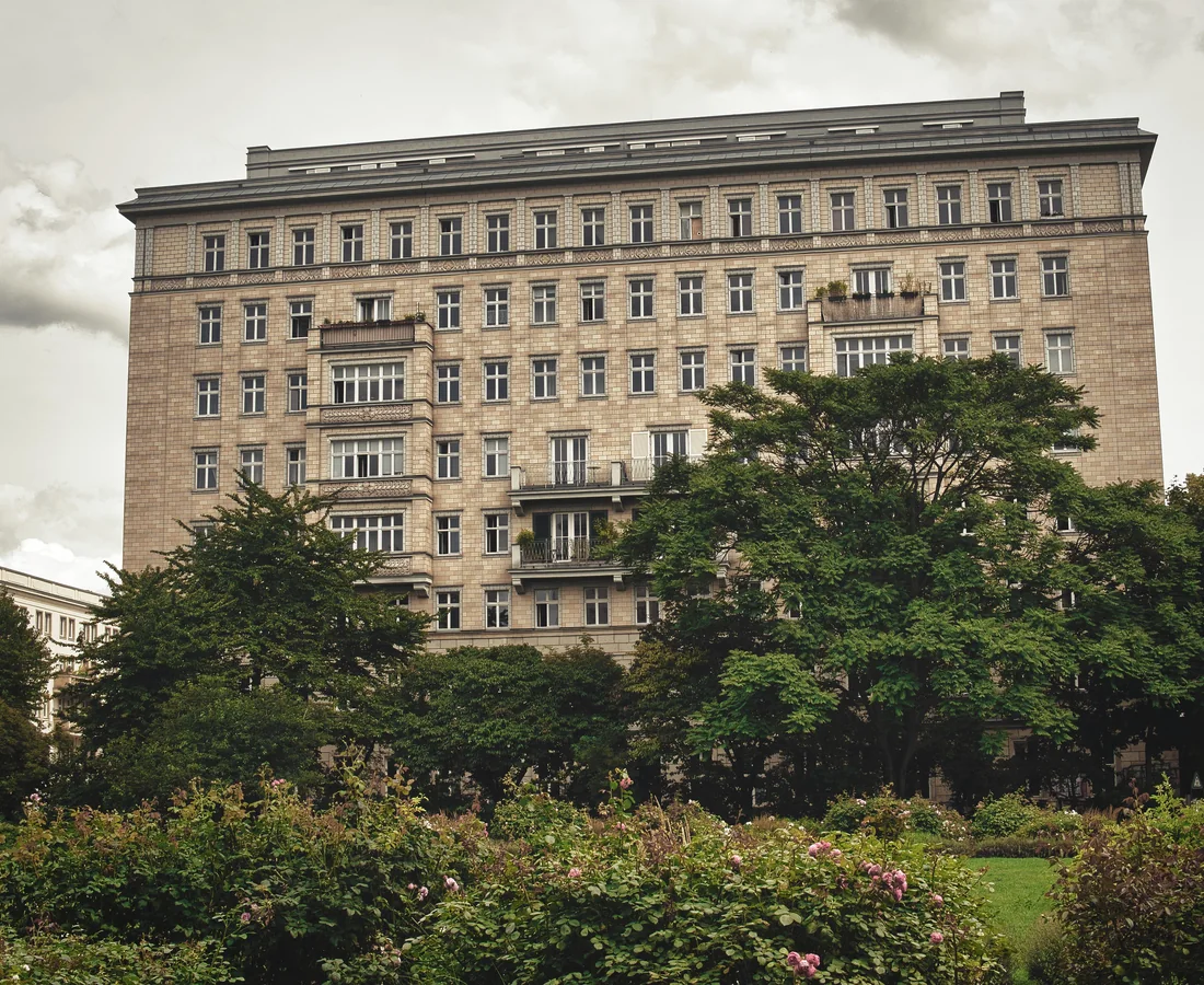 Großes Berliner Wohngebäude steht hinter Bäumen und einer begrünten Parkanlage